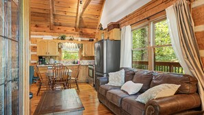A rustic cabin interior with a wooden dining table, leather sofa, and a kitchen area with wooden cabinets and a refrigerator. - Relax on the Quiet Side – Hot Tub & Serenity! (Townsend)