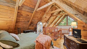 A cozy attic bedroom with a wooden ceiling, a bed with green and white bedding, a dresser, and a television. - Relax on the Quiet Side – Hot Tub & Serenity! (Townsend)