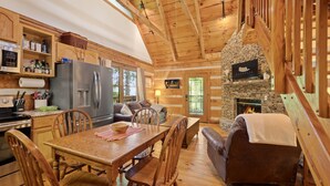 A cozy cabin interior with a dining area, kitchen, and stone fireplace. - Relax on the Quiet Side – Hot Tub & Serenity! (Townsend)
