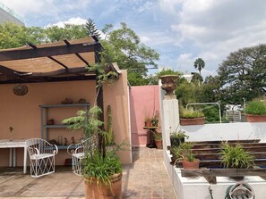 Enjoy the serene rooftop retreat with a table and chairs, surrounded by lush greenery and a staircase to a higher level.