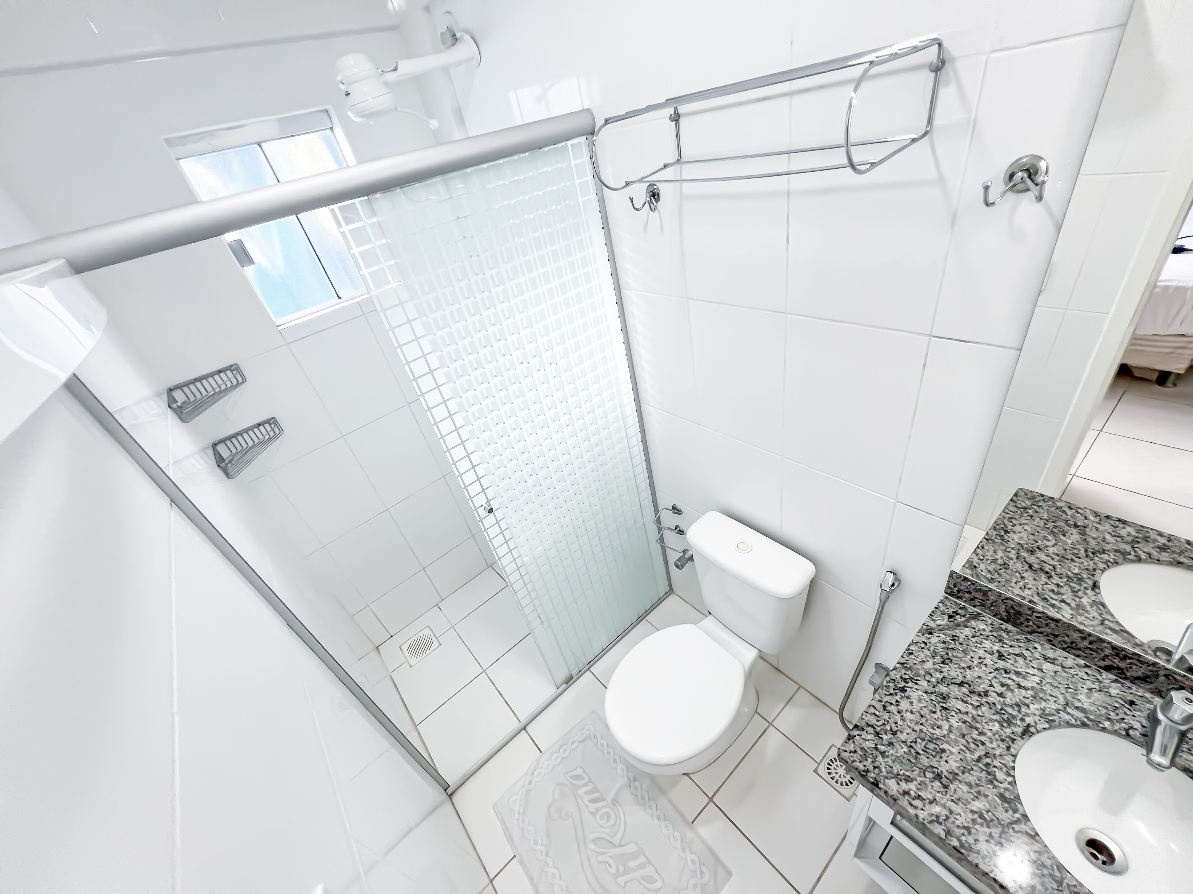 A modern bathroom with a glass shower enclosure, a white toilet, and a granite countertop sink.