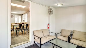 A room with a glass partition separating a dining area with chairs and a table from a seating area with two sofas and a small table. - Cozy Keansburg Cottage: Walk to Beach & Boardwalk! (Keansburg)