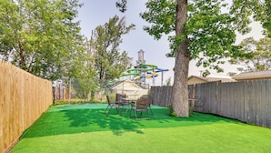 A backyard with artificial green turf, a wooden fence, and a metal slide structure. - Cozy Keansburg Cottage: Walk to Beach & Boardwalk! (Keansburg)