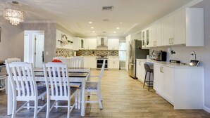 Una cocina moderna con muebles blancos, una isla central y un comedor con sillas blancas.