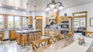 Une cuisine spacieuse dotée de meubles en bois, d’un grand îlot central avec des tabourets et d’un coin repas avec une table et des chaises.