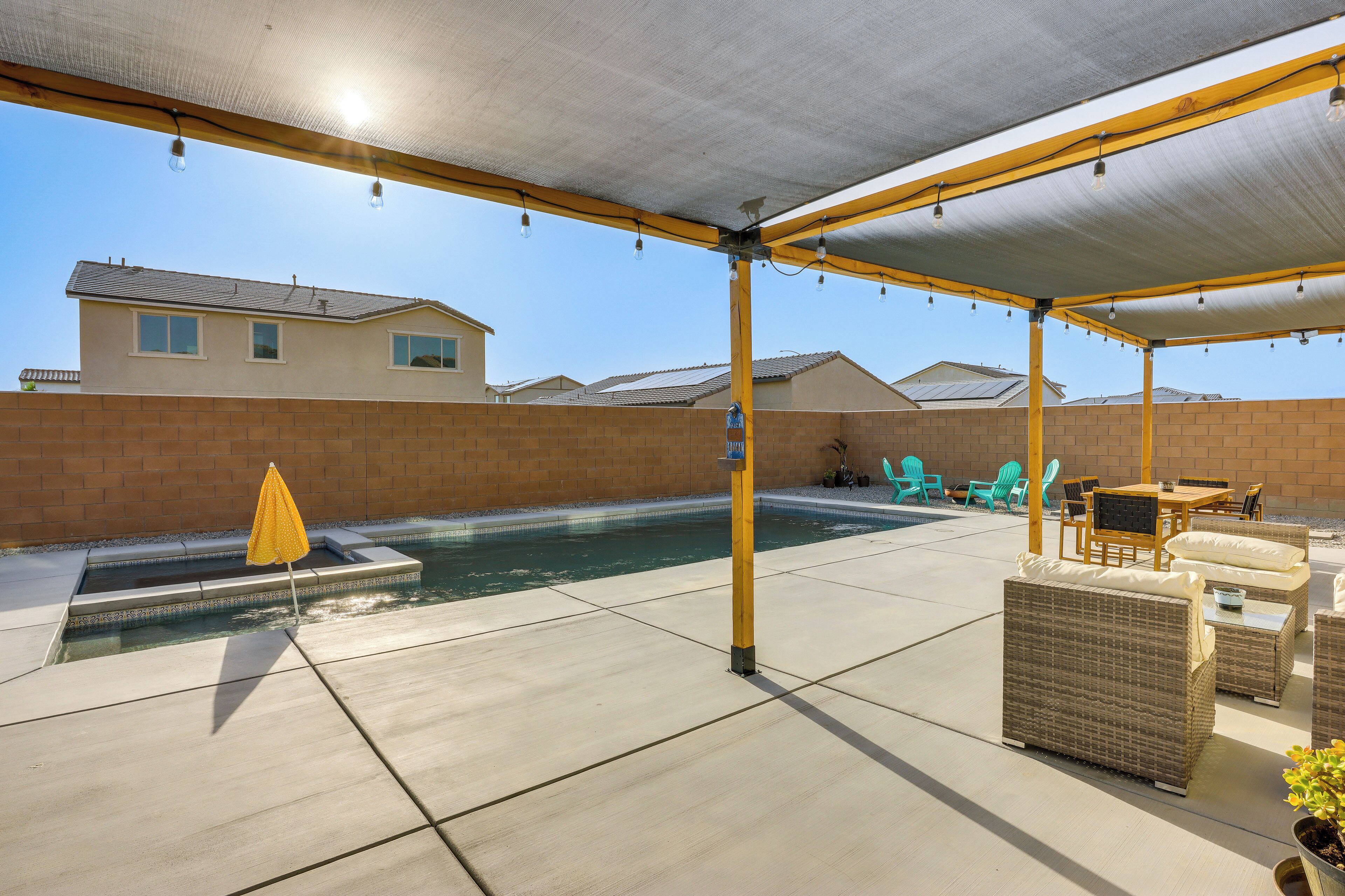 Et overdækket område udendørs med pool, liggestole og en gul parasol.