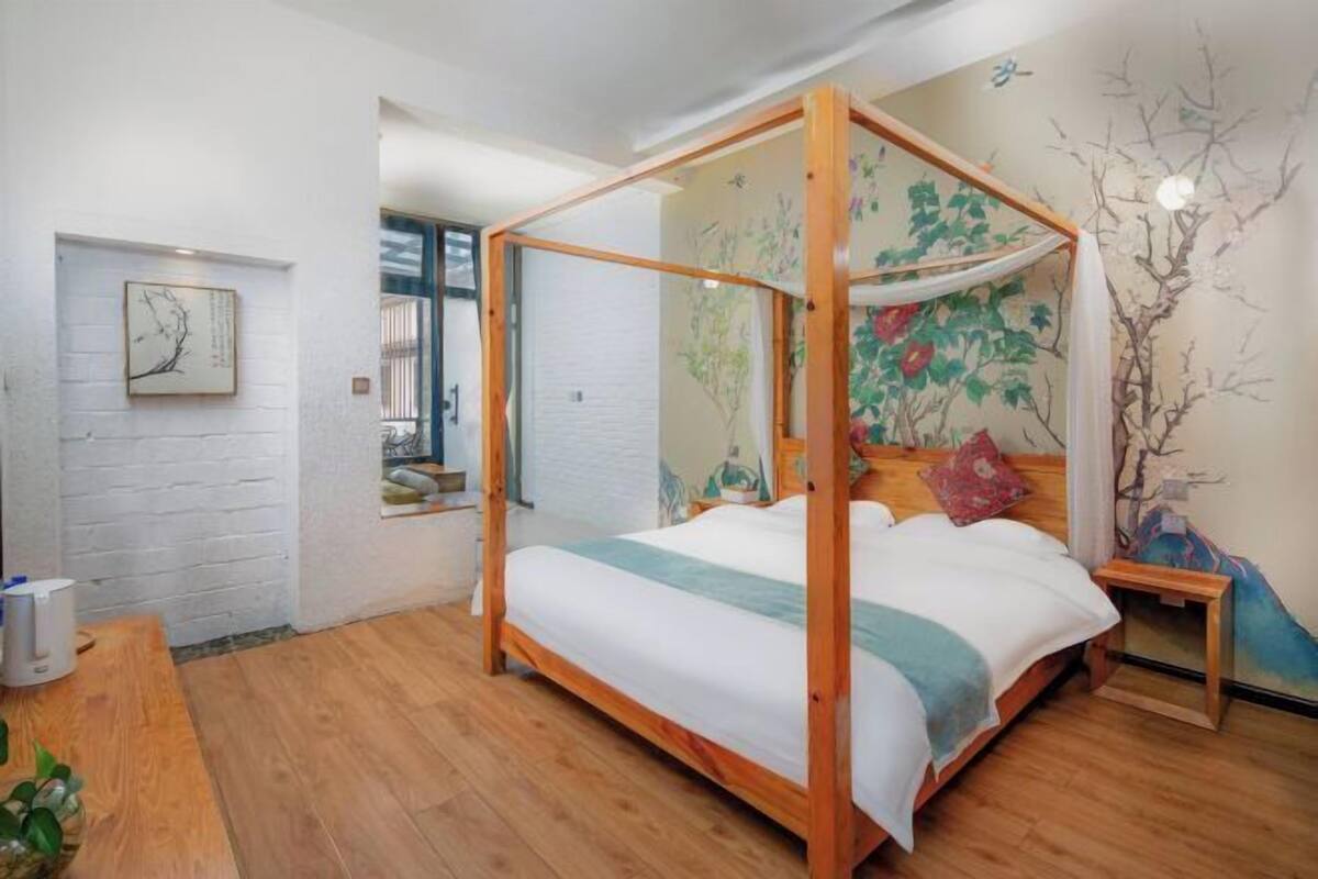A four-poster bed with a canopy, a wooden nightstand, a wall-mounted shelf, and a window with blinds.