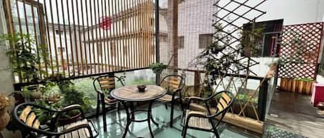 Un balcón con paredes de vidrio, mobiliario exterior, una planta en maceta y vista a un edificio.