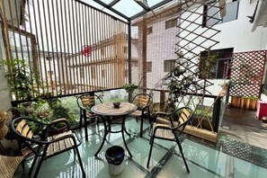 A glass-enclosed balcony with outdoor furniture, a potted plant, and a view of a building. - Buxianshan Guesthouse (Dali City)