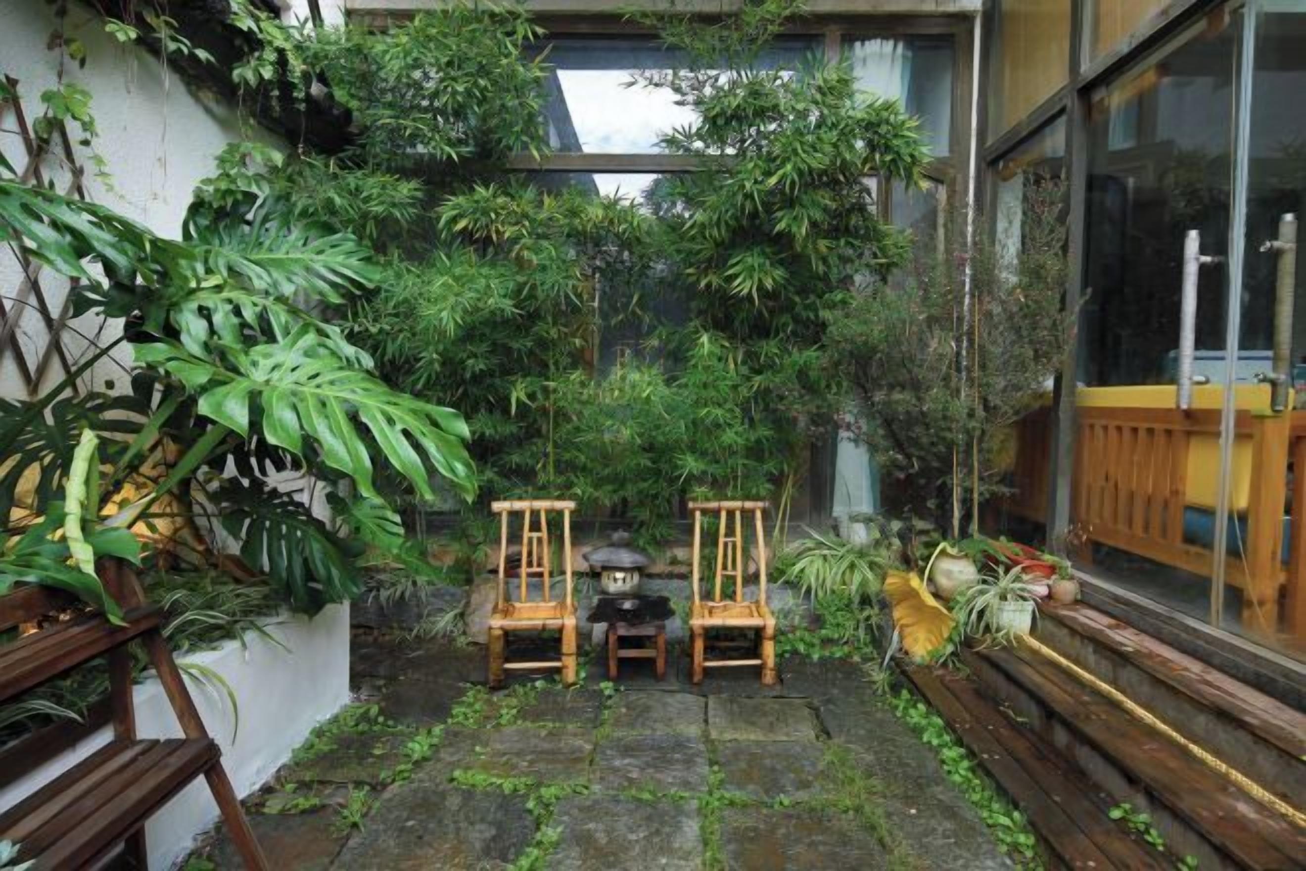 Un pequeño patio con un banco de madera, dos sillas y una mesa.