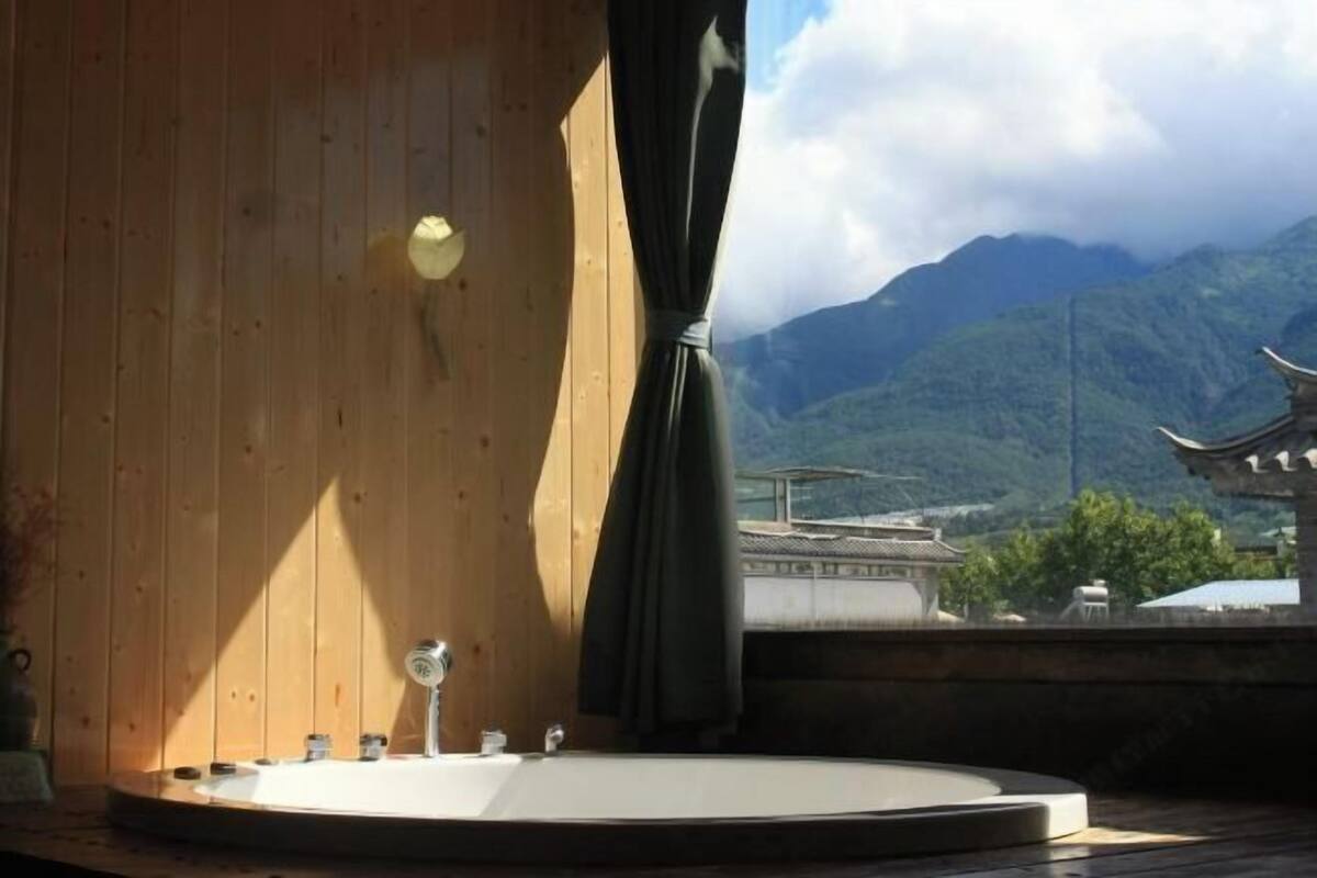 A wooden room with a round bathtub, a window with a view of mountains and traditional architecture.