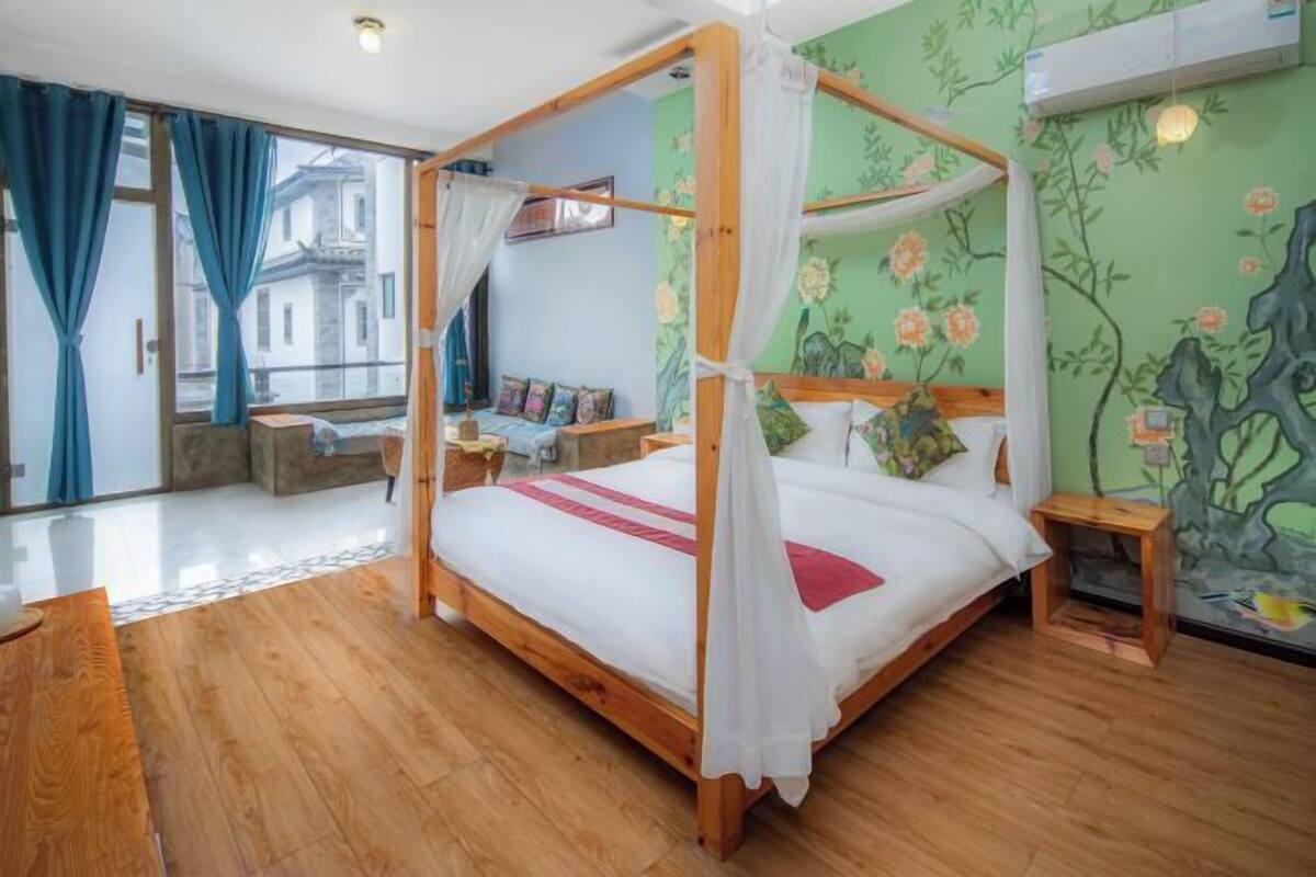 A four-poster bed with a canopy, a wooden floor, a balcony with blue curtains, and a floral wall mural.
