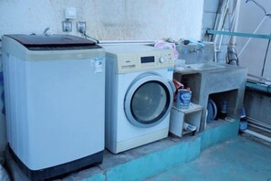 A washing machine and a dryer side by side, with a sink and a hose visible in the background. - Buxianshan Guesthouse (Dali City)