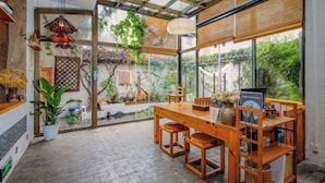 Un comedor amplio con una mesa y sillas de madera, ventanas grandes y plantas colgantes.