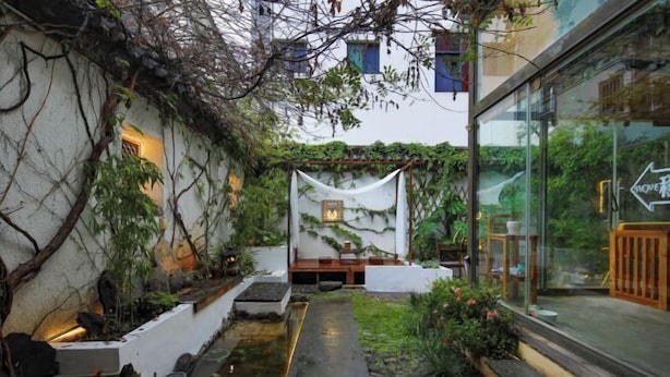 Un sendero estrecho que conduce a una zona de estar con una fuente de agua y una pared blanca decorada con un mural.