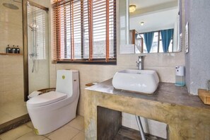 Ein Badezimmer mit Toilette, Waschbecken, Dusche und einem Fenster mit Jalousien.