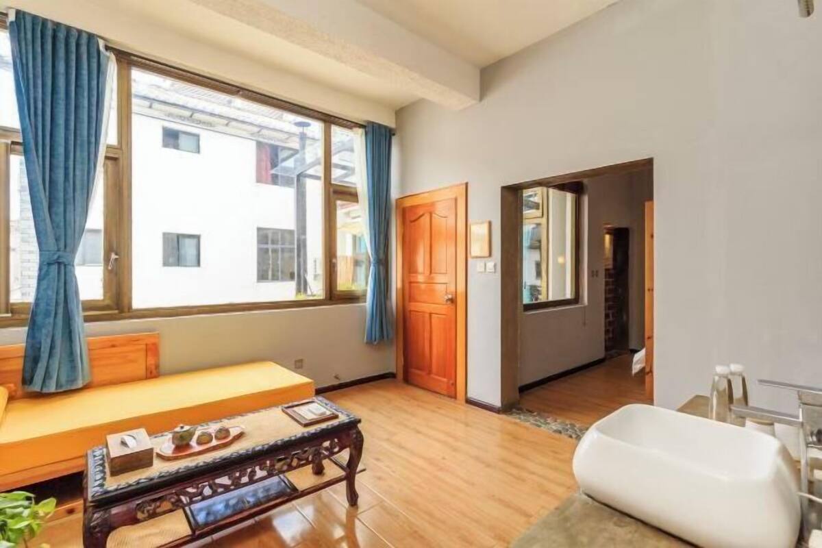 A room with a wooden floor, a sofa, a table with a tray, a bathtub, and a window with curtains.