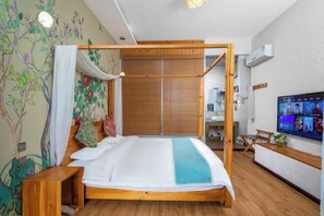 Ein Zimmer mit einem hölzernen Himmelbett, einem an der Wand befestigten Fernseher und einem durch eine Glastür einsehbaren Badezimmer.