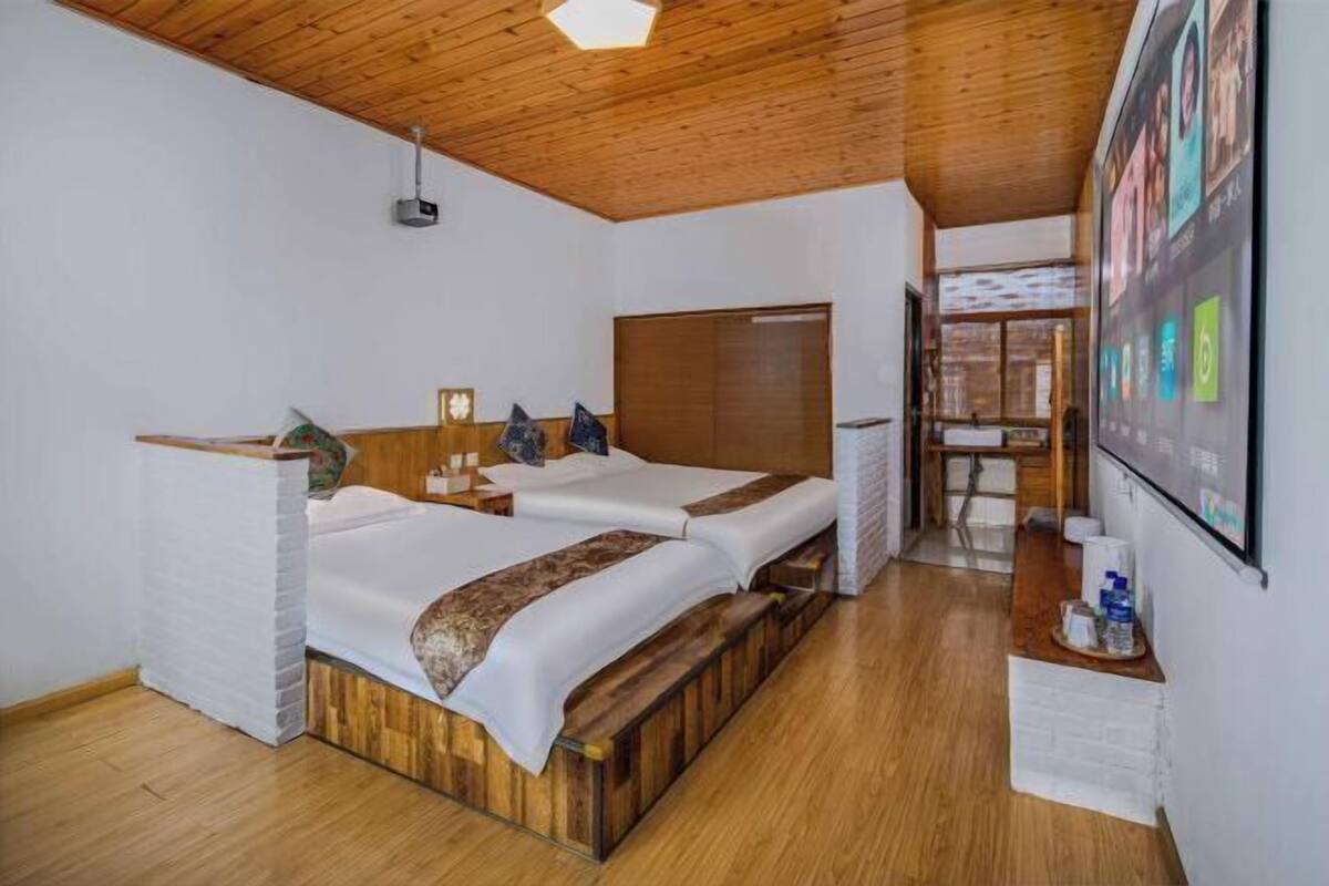 A room with two beds, wooden flooring, a wooden ceiling, a projector, and a wall-mounted screen.