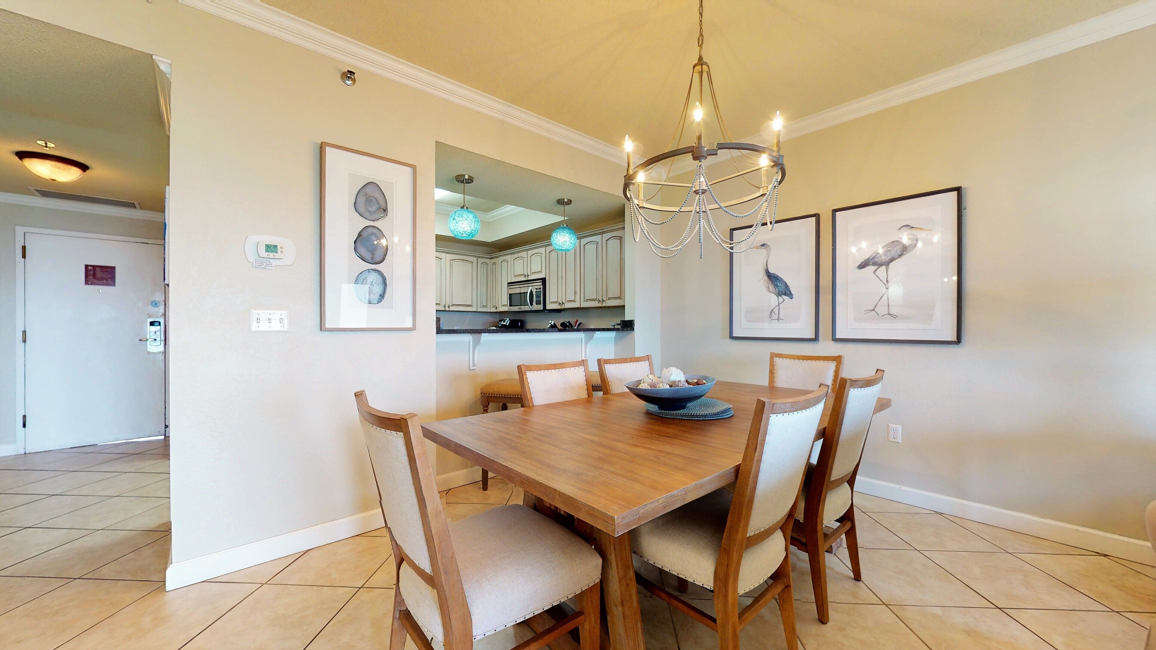 A dining area with a wooden table, six chairs, a chandelier, and framed artwork on the walls.