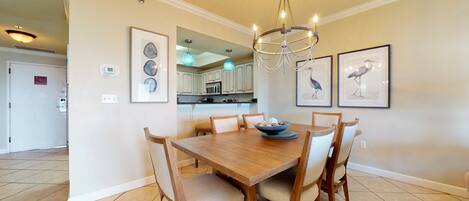 A dining area with a wooden table, six chairs, a chandelier, and framed artwork on the walls.