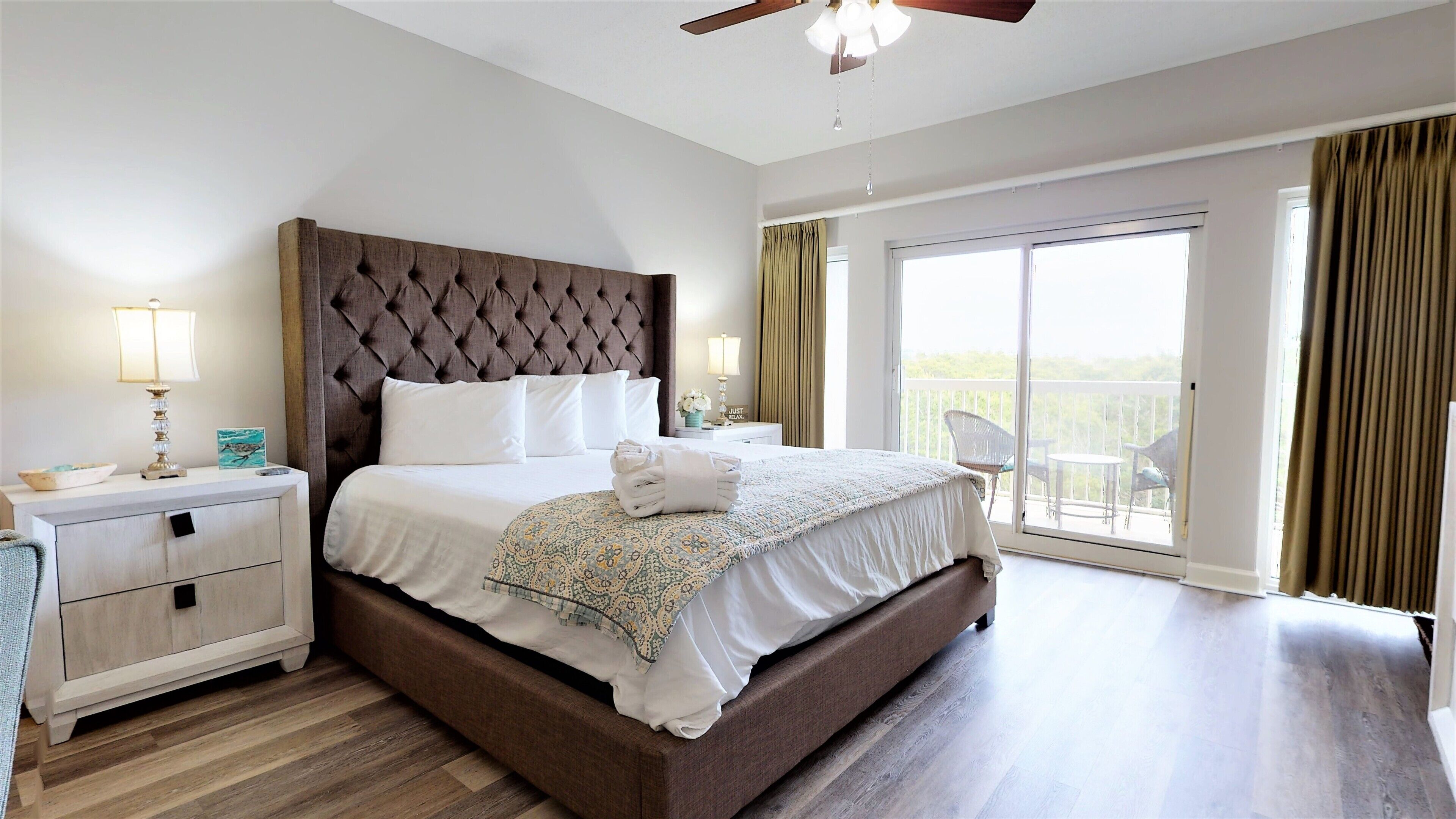 Een slaapkamer met een geborduurde hoofdbord, een groot bed met witte lakens, een nachtkastje met een lamp en uitzicht op een balkon door een schuifdeur.