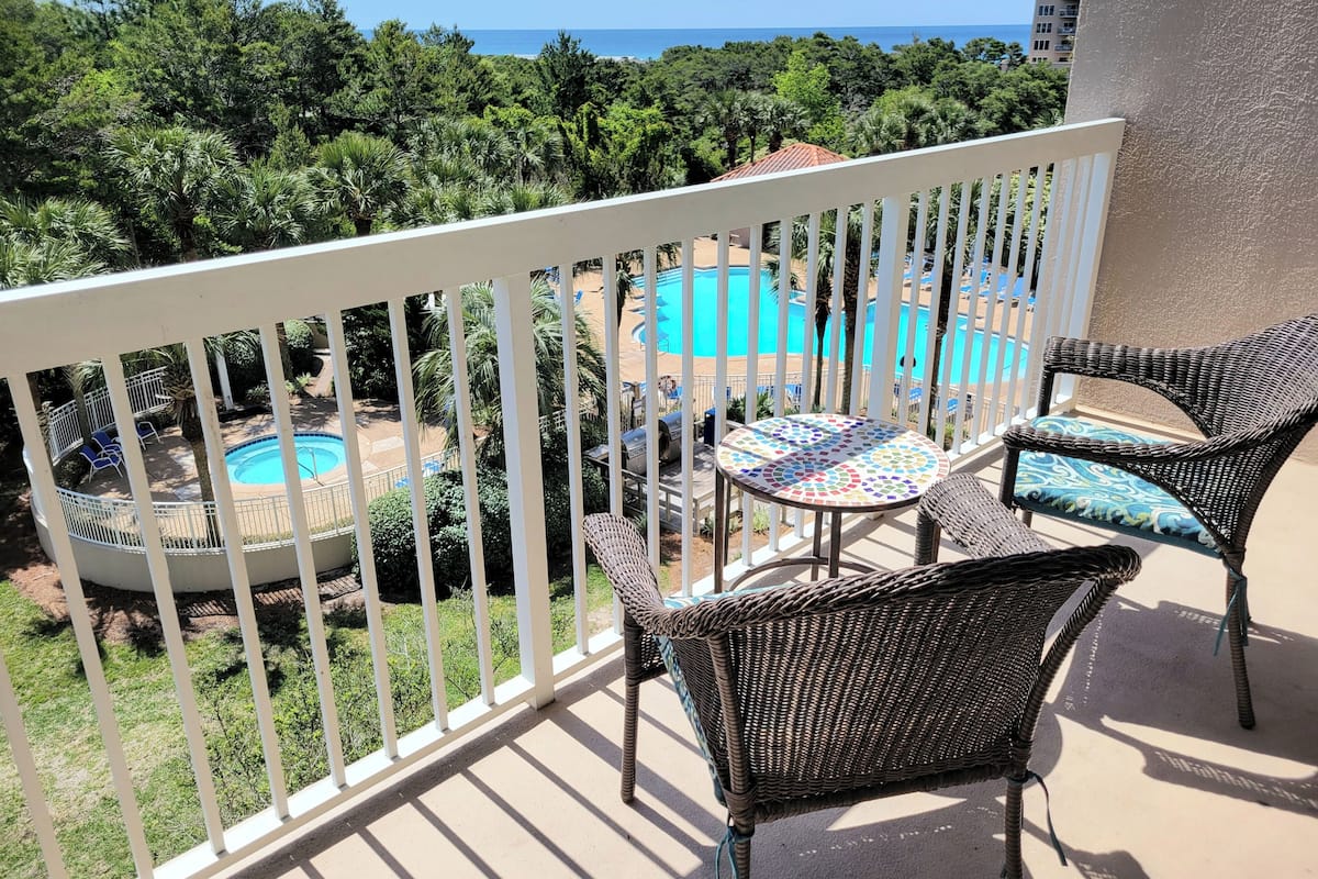 Ein Balkon mit Korbmöbeln, ein Schwimmbad und Blick aufs Meer.