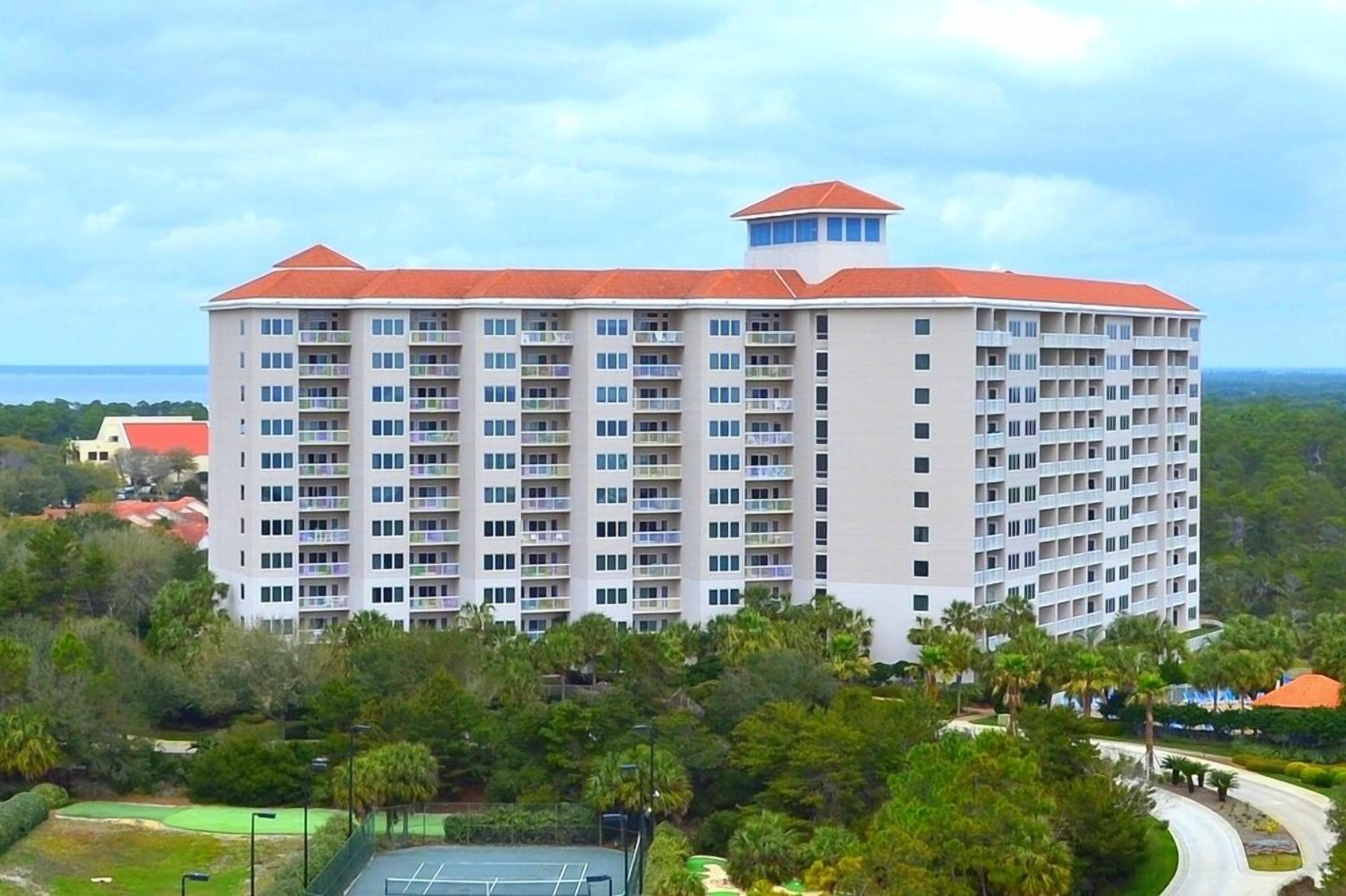 A multi-story hotel with a red roof, surrounded by lush greenery and a golf course.