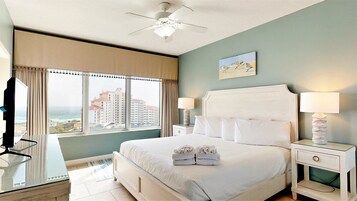 Una habitación de hotel con una cama grande, dos mesitas de noche con lámparas, un ventilador de techo y vistas a edificios a través de la ventana.