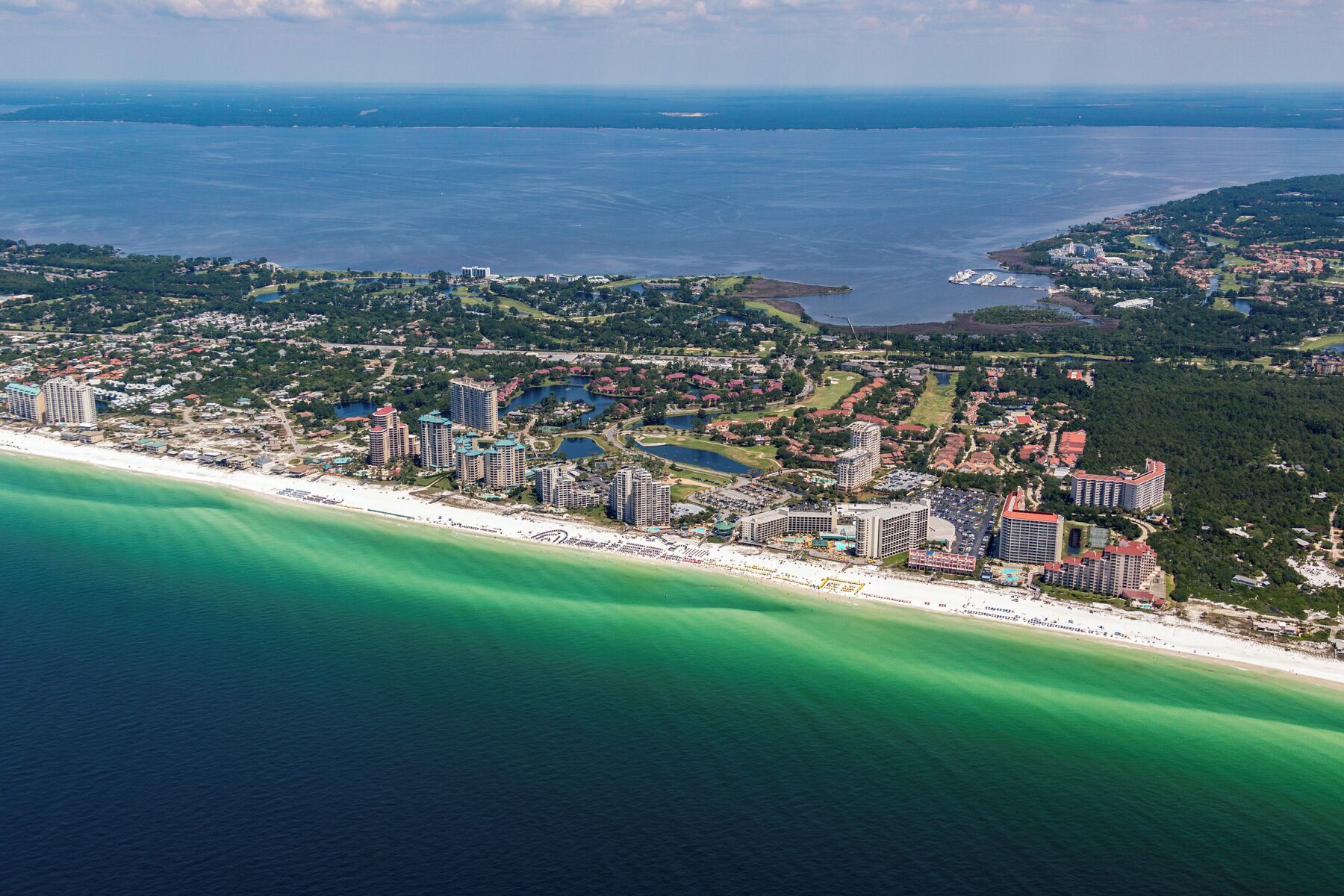 An aerial view of a coastal resort with multiple high-rise buildings, a beachfront, and a large body of water.
