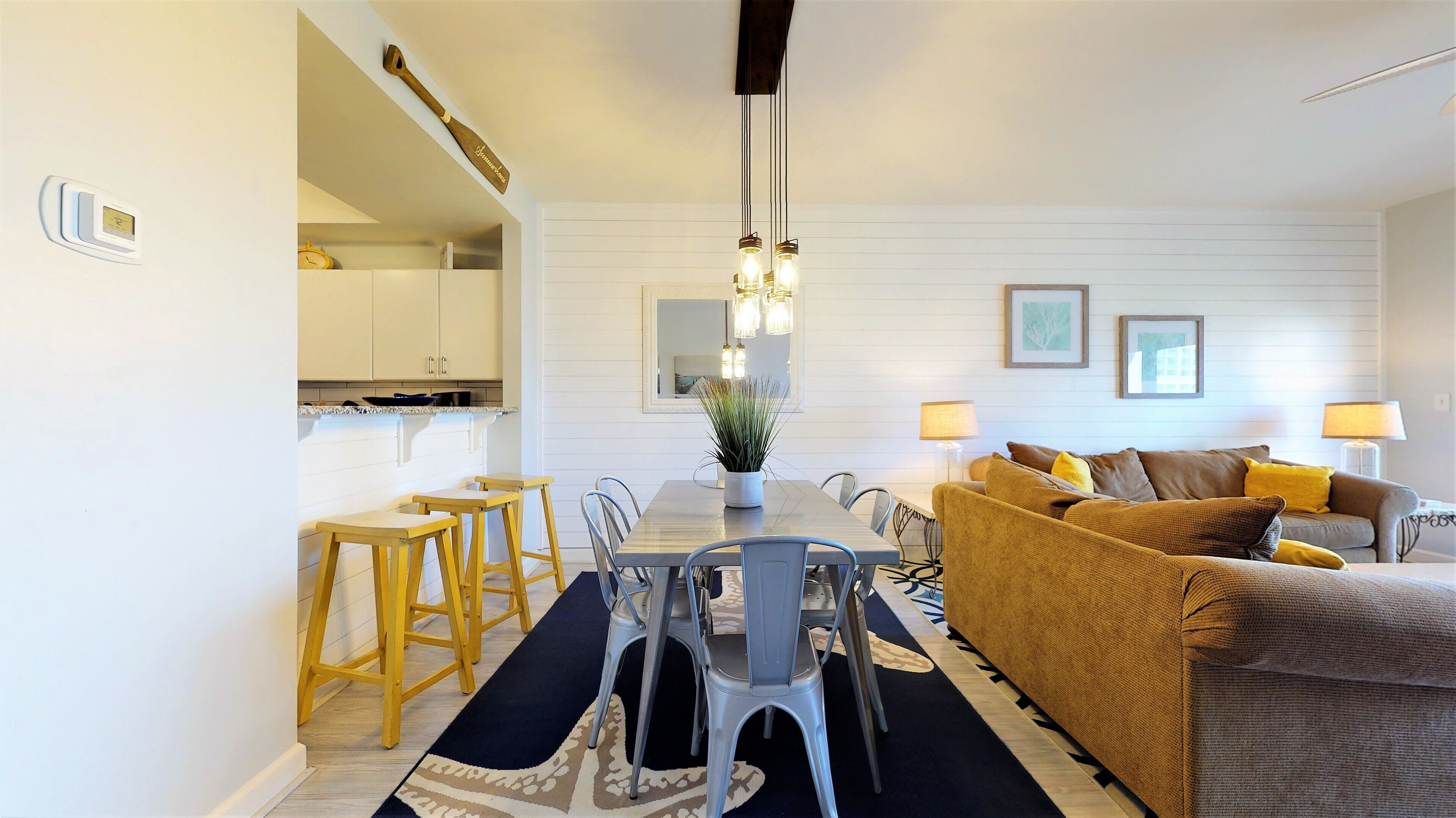 A modern living room with a sofa, coffee table, and dining area with chairs and a plant.