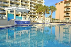 Una piscina con borde de azulejos azules, rodeada por un hotel de varios pisos con balcones y palmeras.