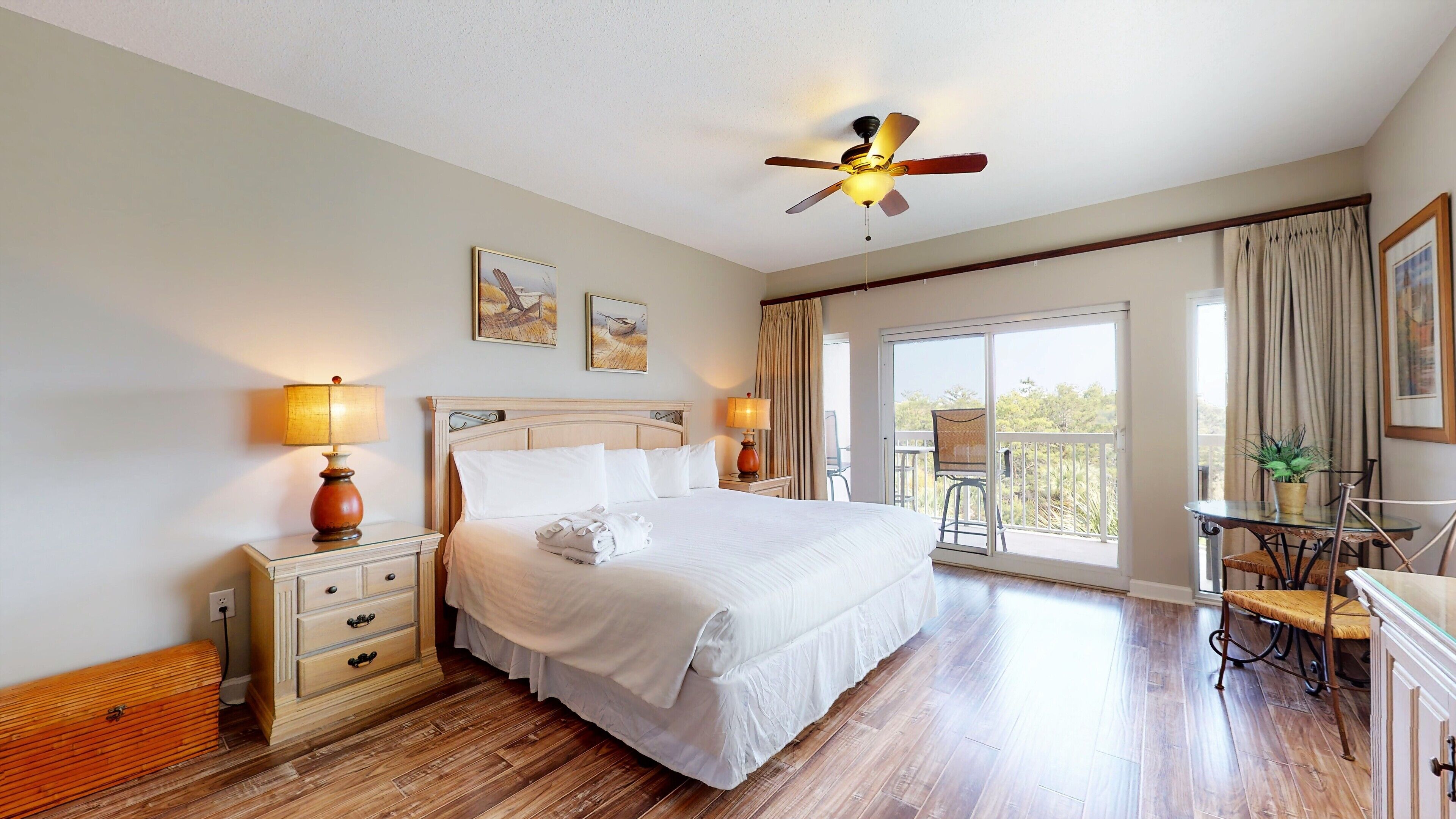 A hotel room with a large bed, a ceiling fan, a balcony with a table and chairs, and a view of the outdoors.