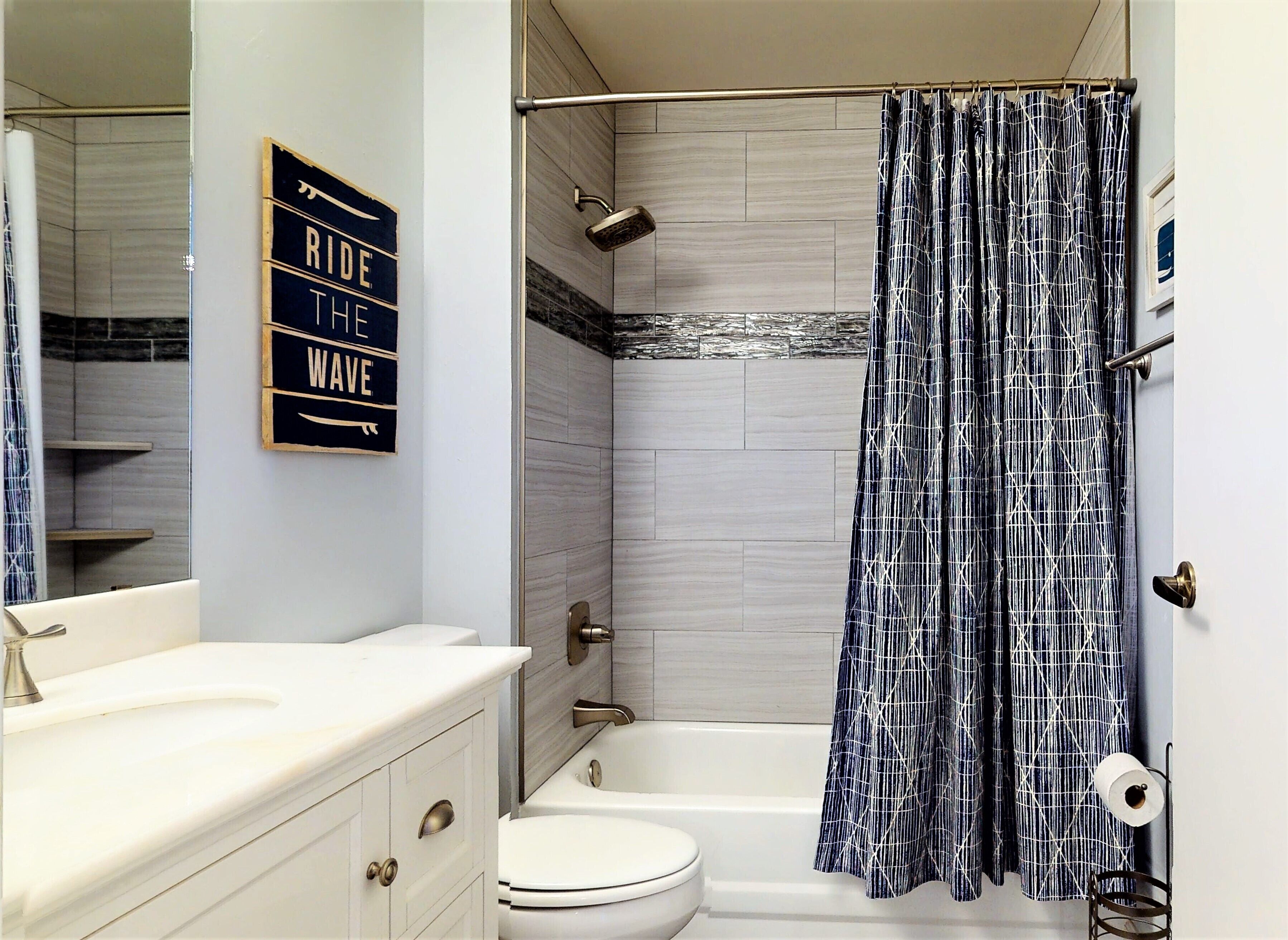 A bathroom with a white vanity, a toilet, a bathtub, and a shower curtain with a geometric pattern.