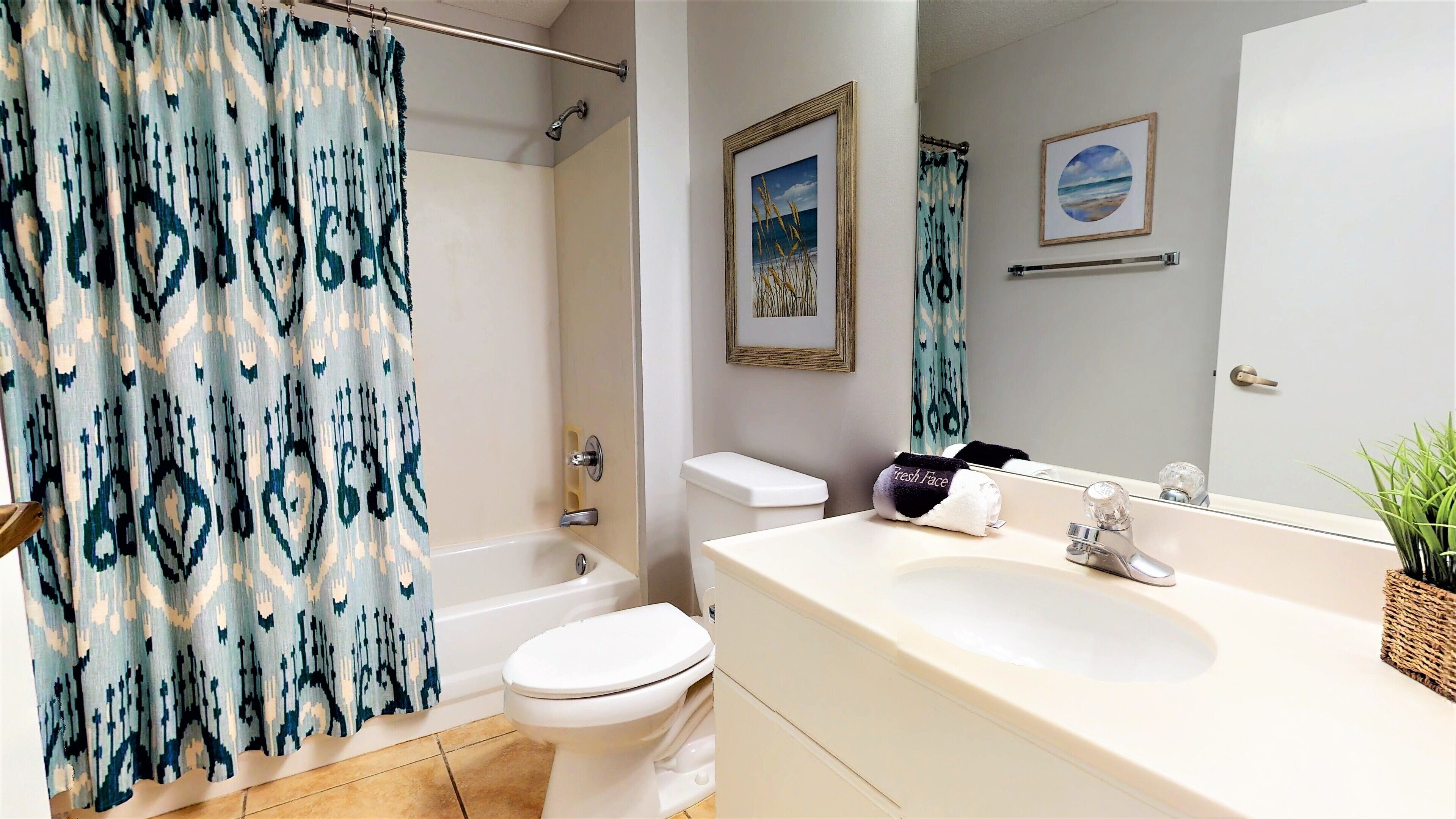 A bathroom with a shower curtain, toilet, sink, and a framed picture on the wall.