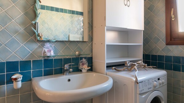 Un baño con un lavamanos blanco, una lavadora y un espejo sobre el lavamanos.
