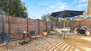 Un espace extérieur aménagé en terrasse, avec une clôture en bois, une table et des chaises, un barbecue et des plantes en pot.