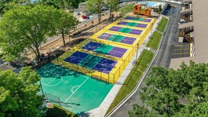 Eine Luftaufnahme eines Sportkomplexes mit mehreren Tennisplätzen, einem Schwimmbecken und einer Brücke im Hintergrund.