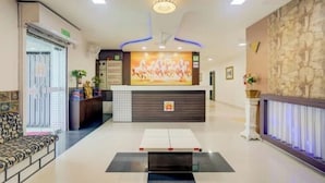 A hotel reception area with a modern design, featuring a reception desk, seating area, and a large wall-mounted TV. - Hotel Ayaansh (Vadodara)