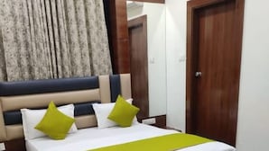 A hotel room with a large bed, a wooden headboard, a mirror, a wardrobe, and an air conditioning unit. - Hotel Ayaansh (Vadodara)
