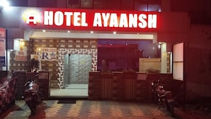 The exterior of Hotel Ayaanash with a prominent red sign, a glass entrance, and two motorcycles parked in front. - Hotel Ayaansh (Vadodara)