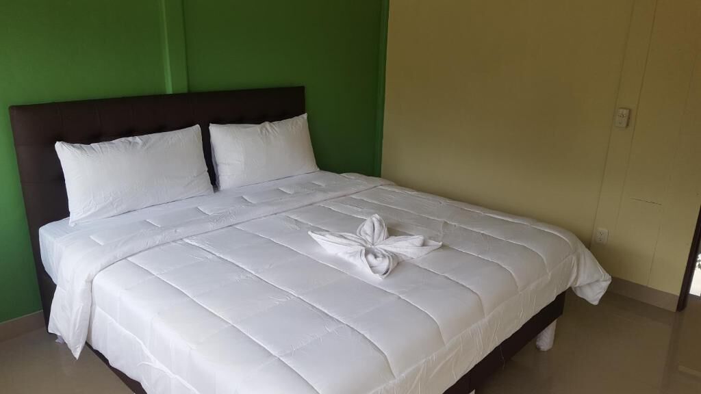 A neatly made bed with white linens and a decorative pillow arrangement in a room with green and beige walls.