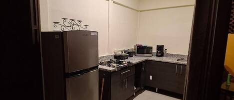 Cocina compacta con refrigerador, microondas, estufa y armarios oscuros.