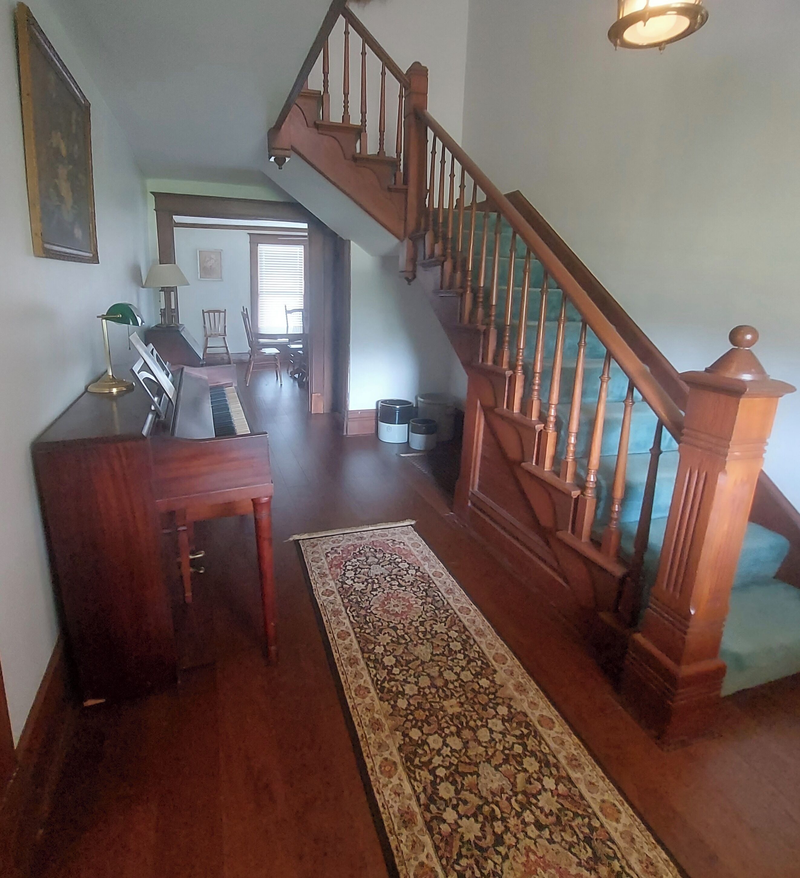 A spacious living area with a wooden staircase, a long patterned rug, and a desk with a lamp.