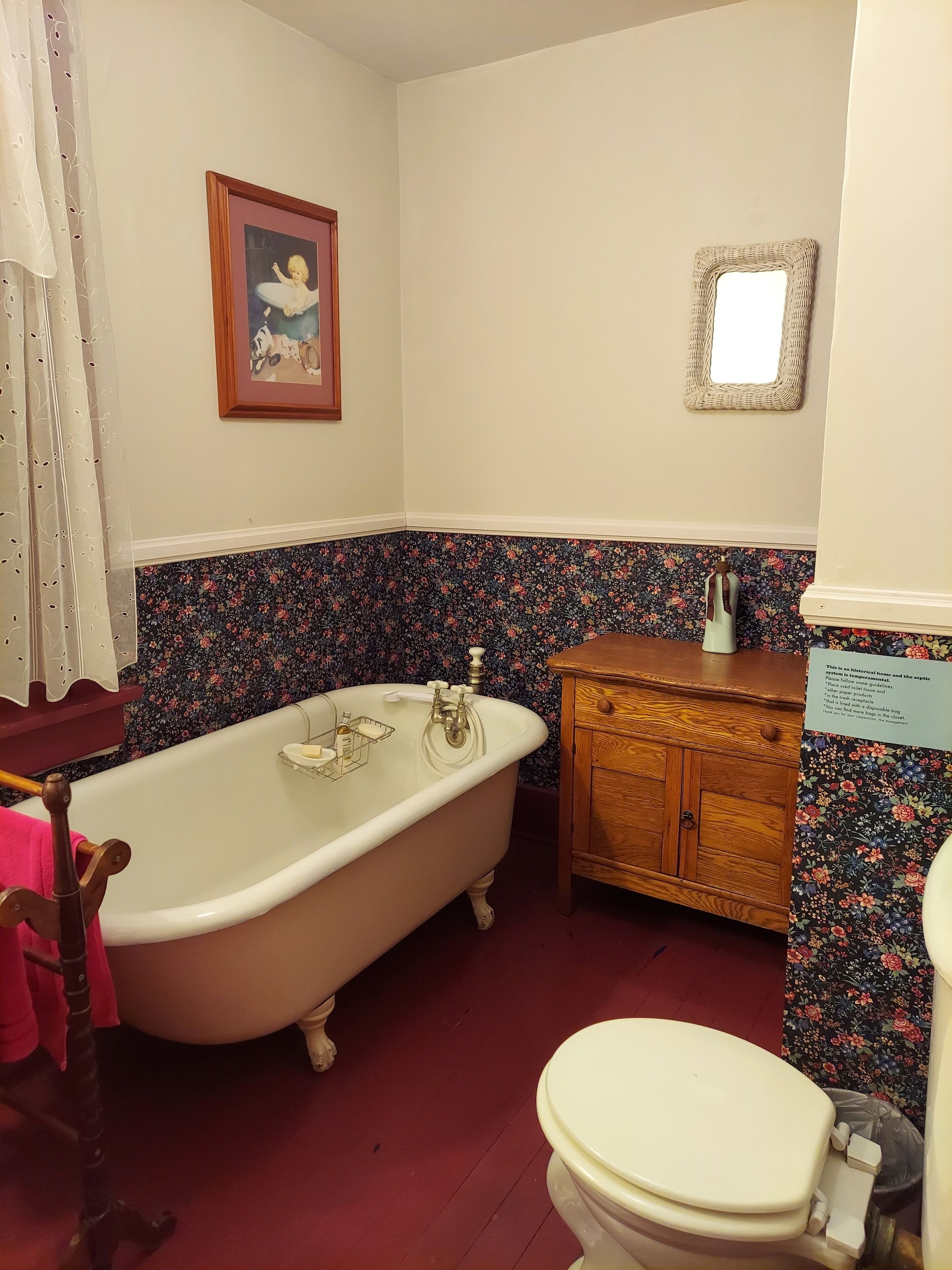 Une salle de bain avec une baignoire sur pieds, un meuble en bois, des toilettes et un papier peint à motifs floraux.