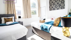 A hotel room with two beds, a large window with curtains, a wall-mounted artwork, and a bedside table with a lamp. - Wesley Chambers By REDWOOD STAYS (Farnborough)
