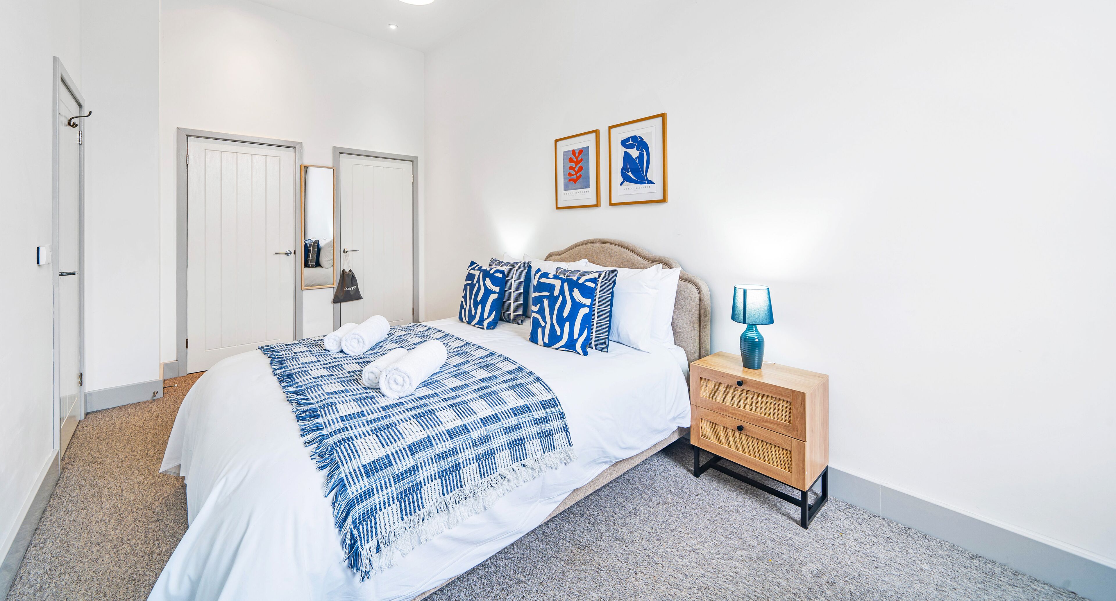 A bedroom with a bed, bedside tables, a wardrobe, and a framed artwork on the wall.