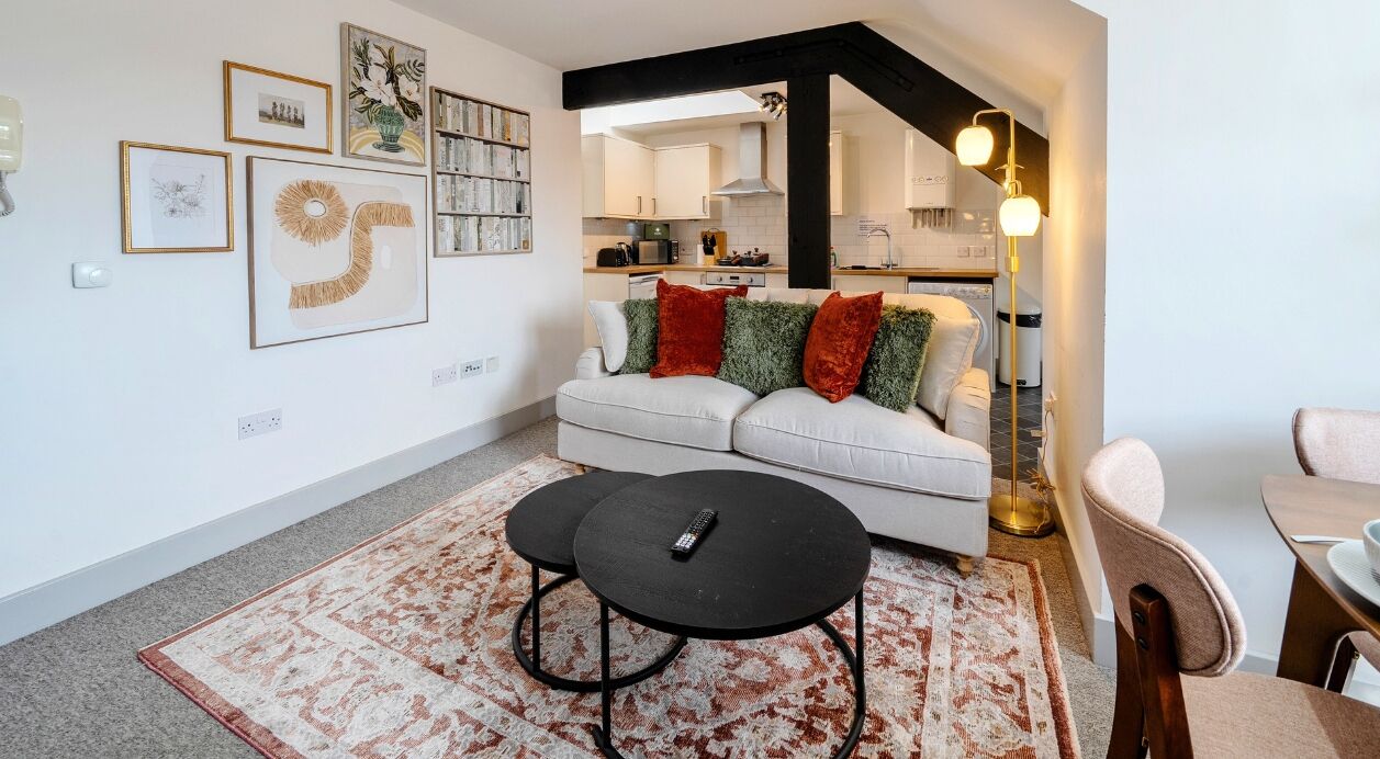 Ein Wohnzimmer mit einer Couch, zwei schwarzen Couchtischen und einem gemusterten Teppich.