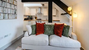A modern living room with a white sofa, red and green cushions, a floor lamp, and a kitchen in the background. - Wesley Chambers By REDWOOD STAYS (Farnborough)
