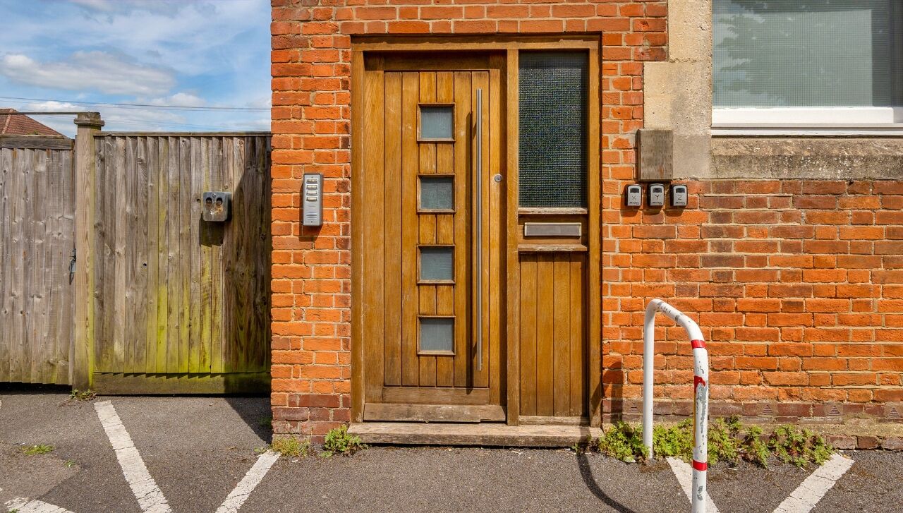 A wooden door with a small window, a metal gate, and a brick wall.